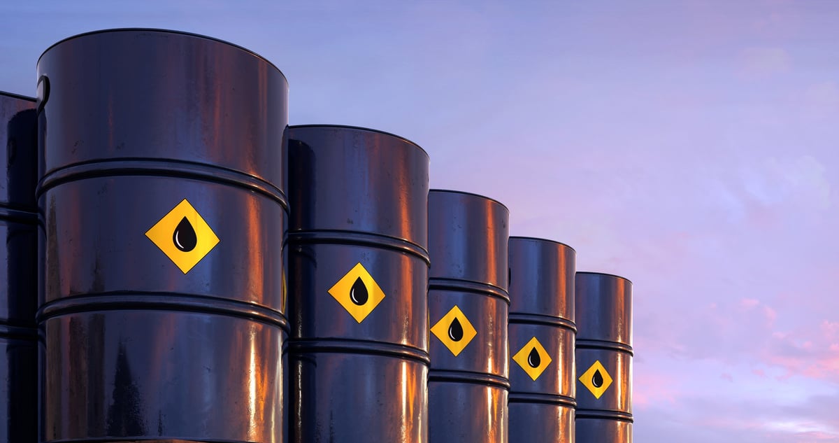 Row of oil barrels in industrial setting under sunset sky